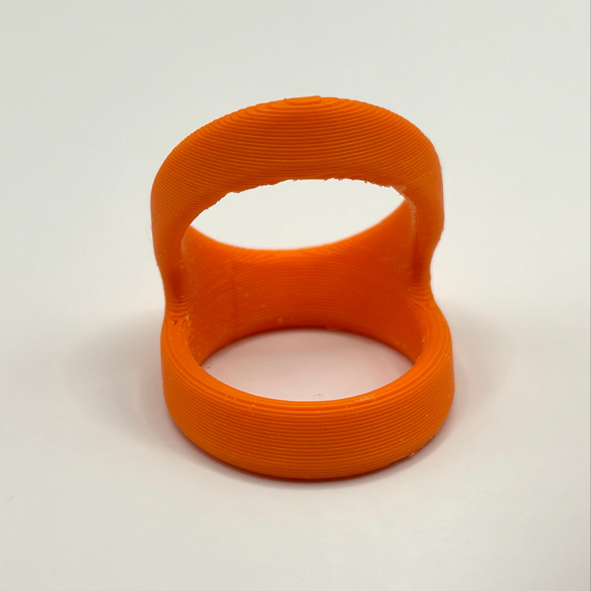 An orange 3D-printed ring with a unique looped design, shown on a neutral light gray background.