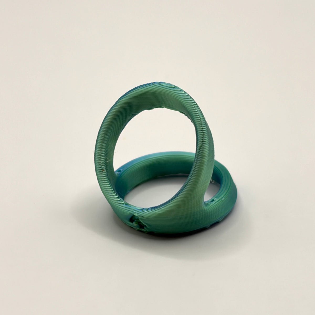 A 3d printed ring n a metallic teal green color, displayed on a neutral light gray background.