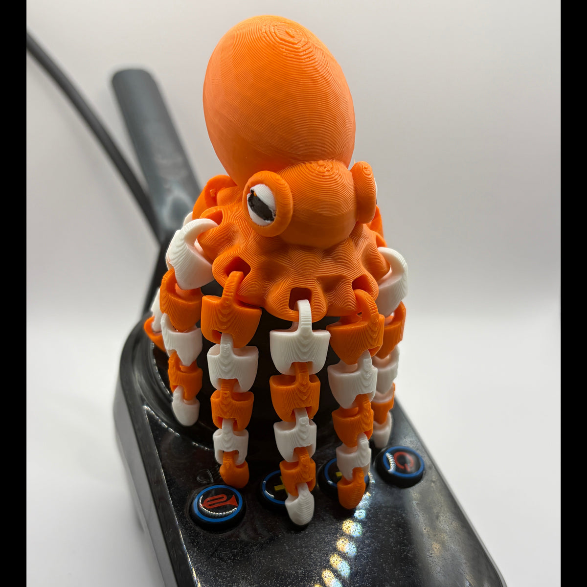A 3D-printed orange octopus-shaped knob on a black console with blue buttons, photographed on a white background.