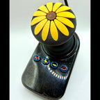 A custom black joystick controller featuring a round daisy-shaped knob with bright yellow petals and a brown center, set against a plain white background.