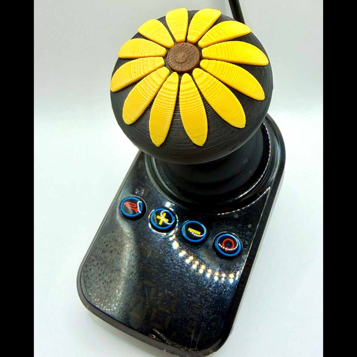 A custom black joystick controller featuring a round daisy-shaped knob with bright yellow petals and a brown center, set against a plain white background.
