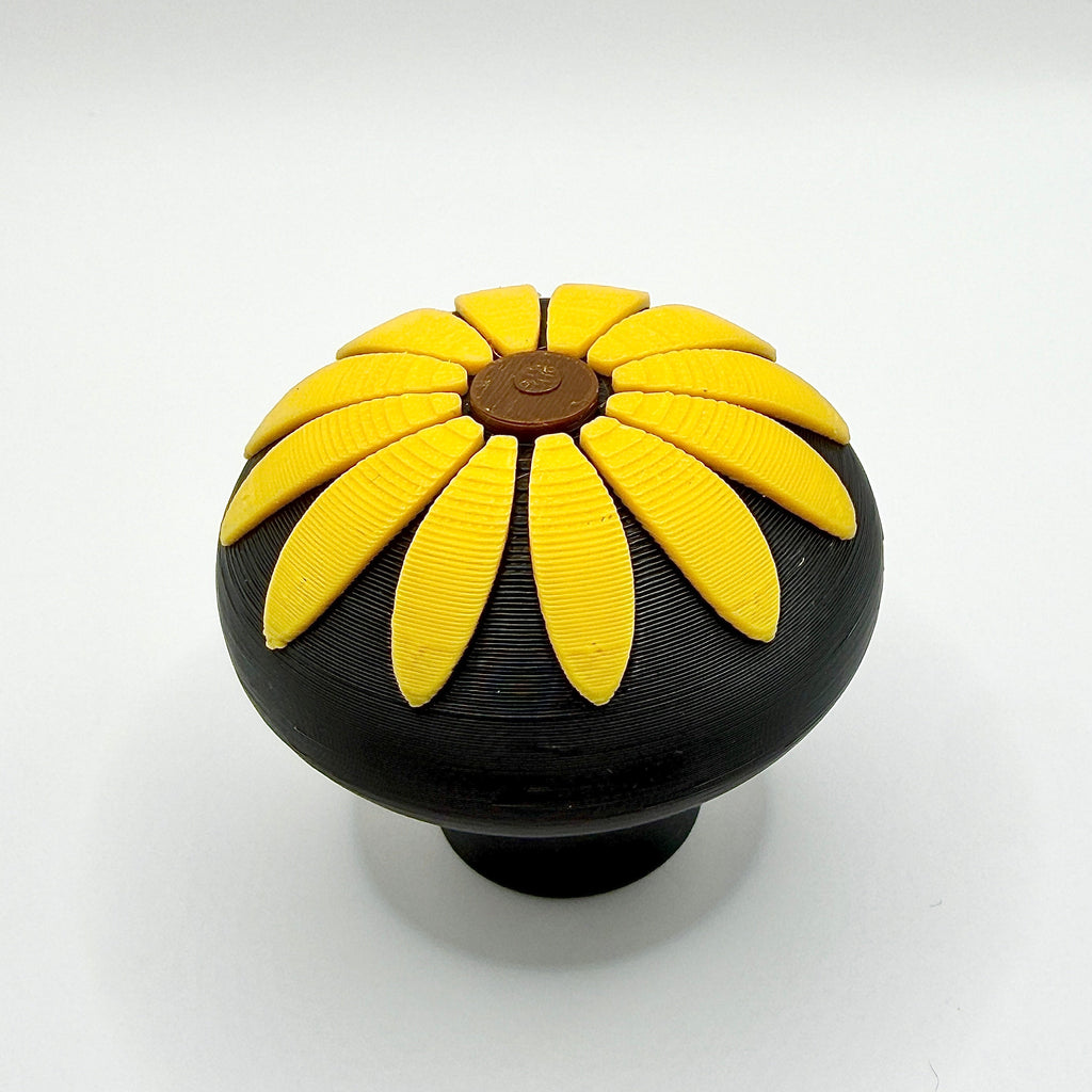 A round black knob featuring a raised sunflower flower design on top, set against a plain white background.