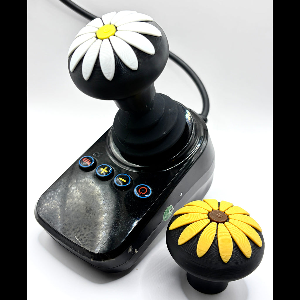 A black joystick controller with a daisy flower knob on top, shown alongside a matching black knob featuring yellow flower petals and a brown center, on a white background.