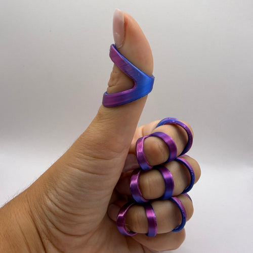 A hand giving a thumbs-up while wearing metallic finger rings in a purple-to-blue gradient finish against a plain light gray background.