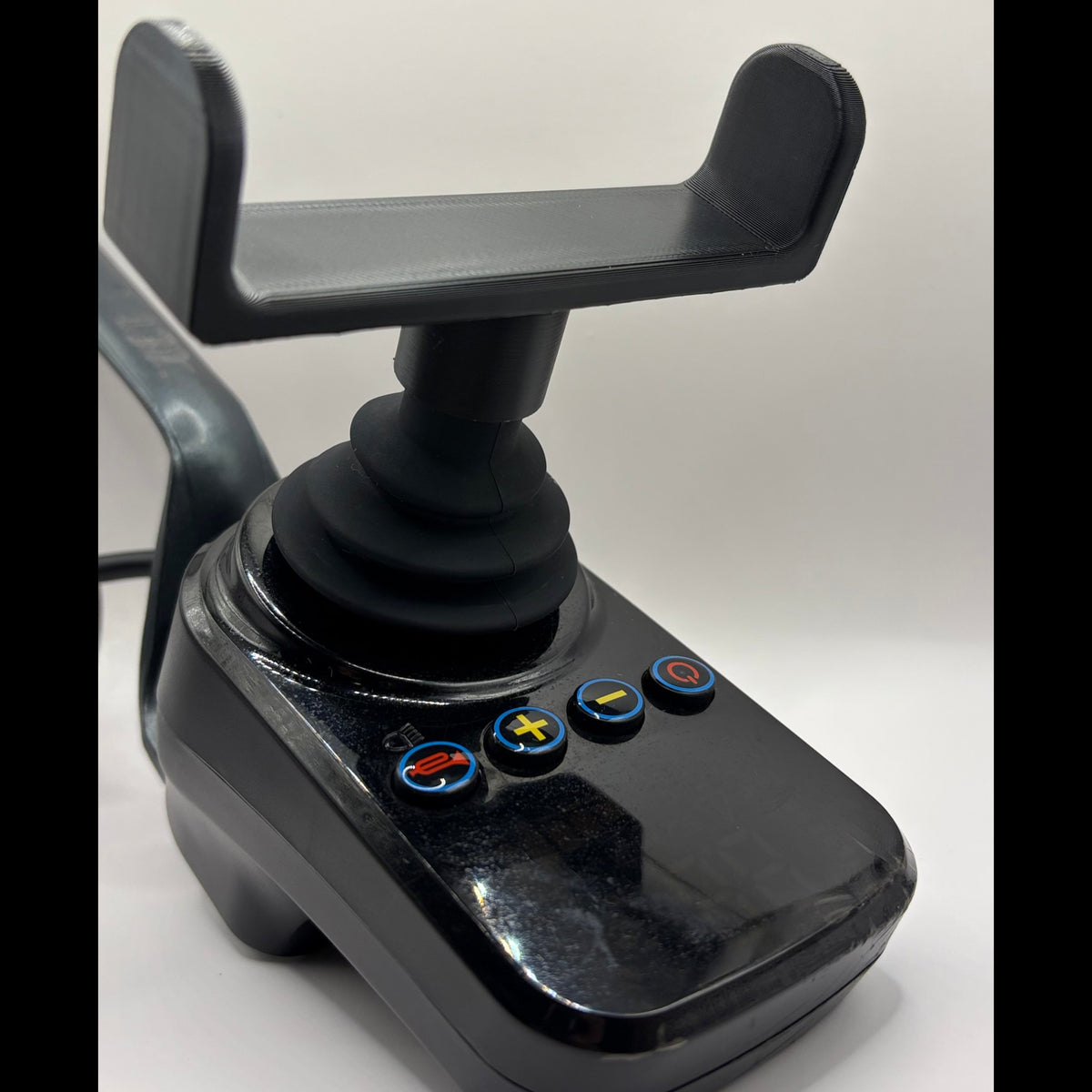 A black plastic joystick control module with a mounting bracket on top and four blue-rimmed buttons on the front face, photographed against a plain light background.