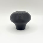 A single matte black knob or handle with a rounded, mushroom-like shape and subtle concentric ring texture on top, photographed against a clean white studio background.
