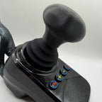 A black joystick control with a textured mushroom shaped grip and four blue buttons featuring red, yellow, and green symbols, shown on a white background.