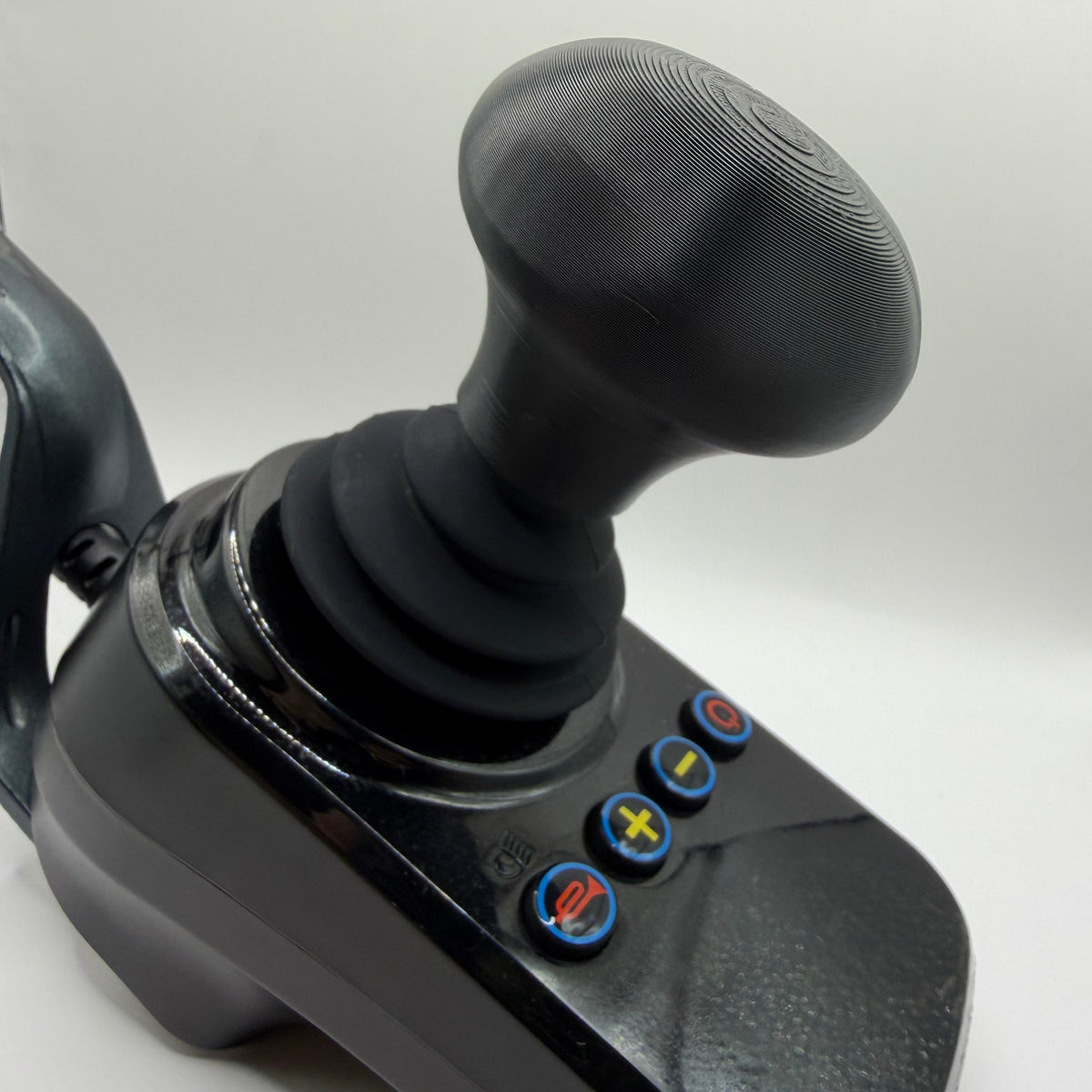 A black joystick control with a textured mushroom shaped grip and four blue buttons featuring red, yellow, and green symbols, shown on a white background.