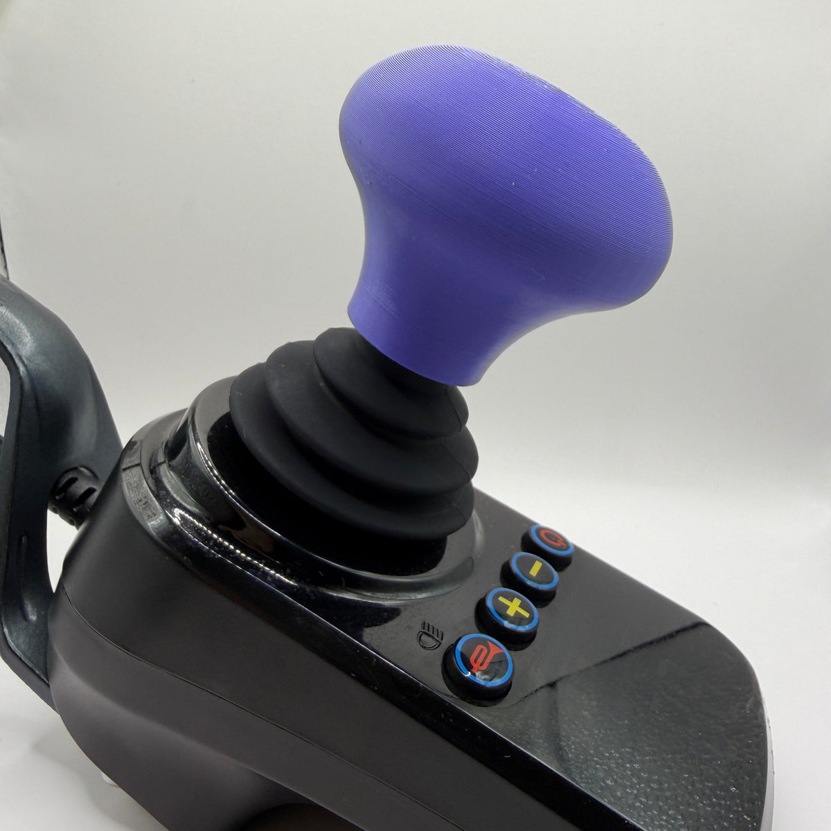 A black joystick control with a purple knob and small blue, red, and yellow buttons on the side, photographed on a plain light background.