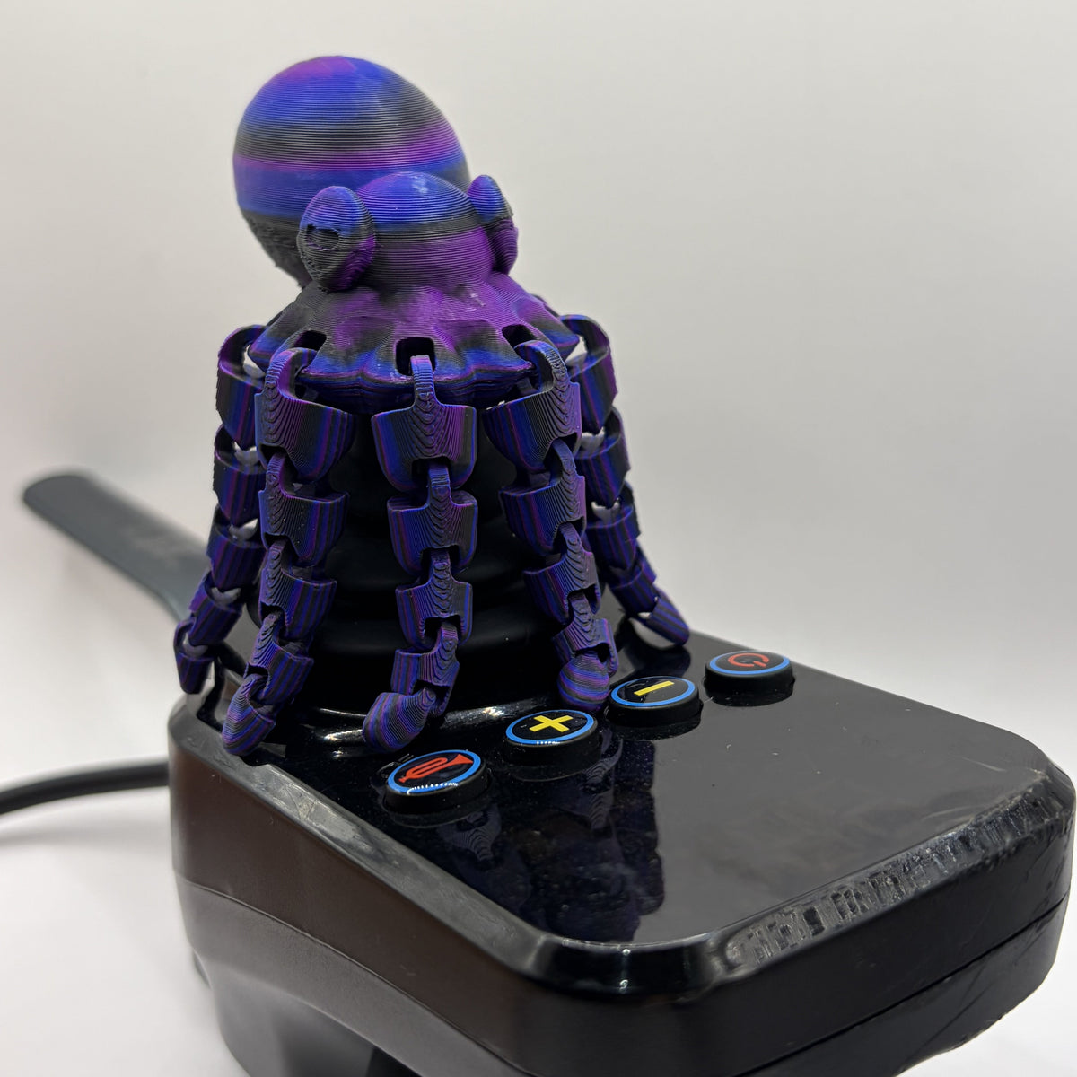 A joystick stick with a purple and blue octopus decoration on the top, featuring multiple button controls on a black base against a plain white background.