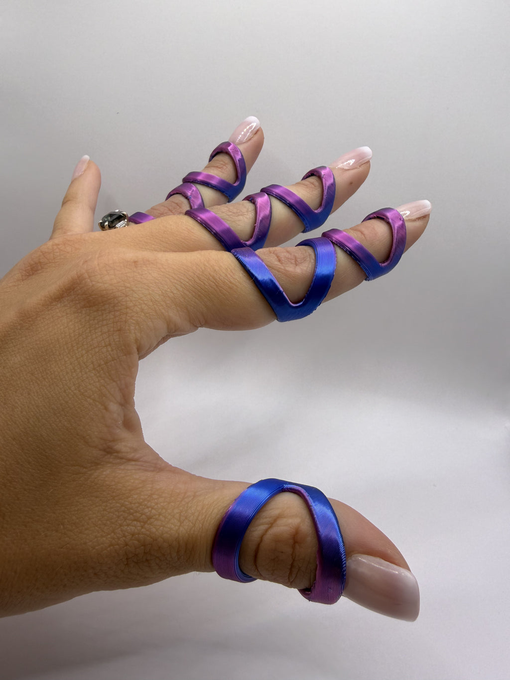 A hand wearing satin finger rings in purple and blue, photographed against a plain light gray studio background.